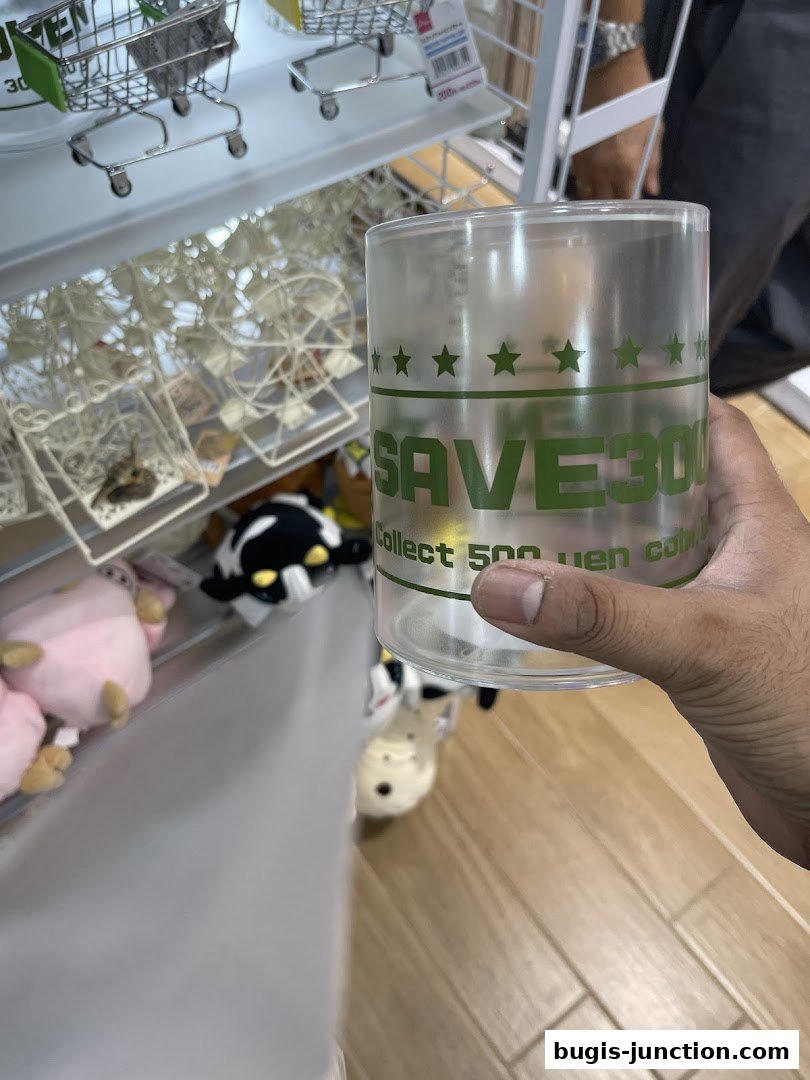A hand holds a clear savings jar with 'SAVE 300' printed on it, in a shop.