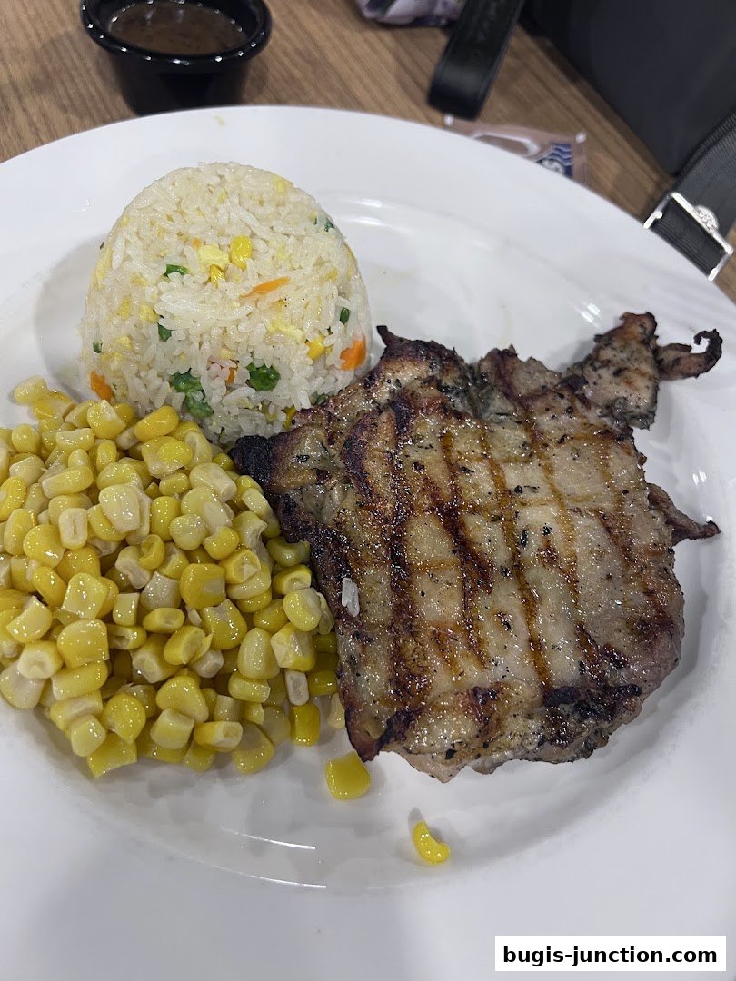A grilled pork chop served with fried rice and corn on a white plate.