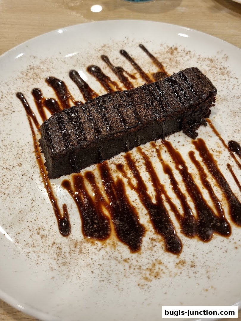A rich chocolate dessert served on a white plate with chocolate sauce and cinnamon.
