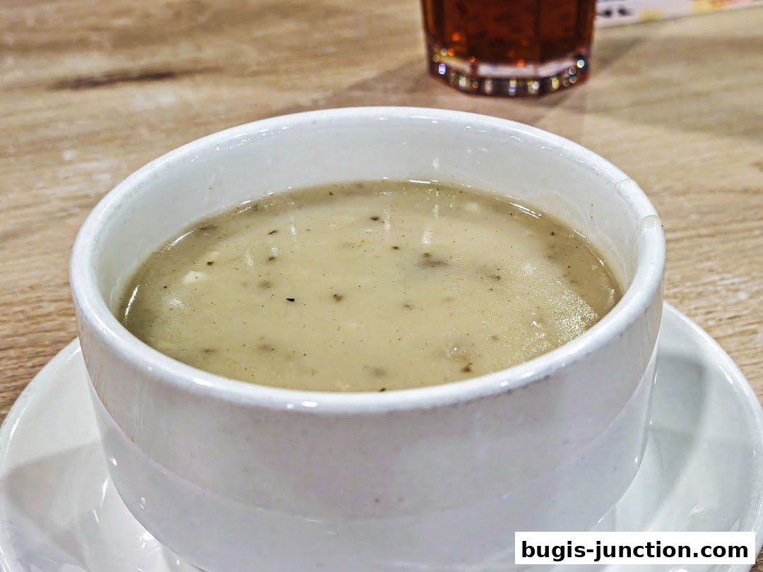 A close-up shot of a bowl of creamy mushroom soup with a glass of iced tea in the background.