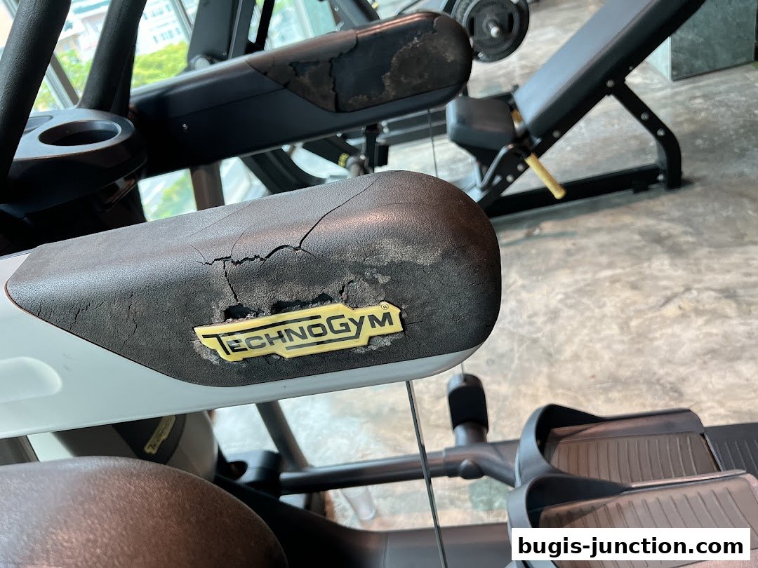 Close-up of a worn Technogym elliptical machine handle with a weight bench in the background.
