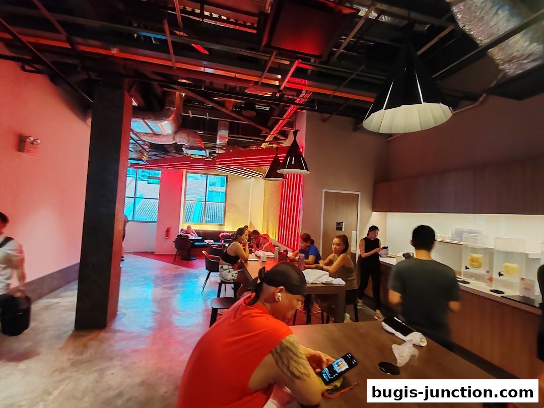 People relaxing and working at tables inside a modern fitness center with red and industrial lighting.