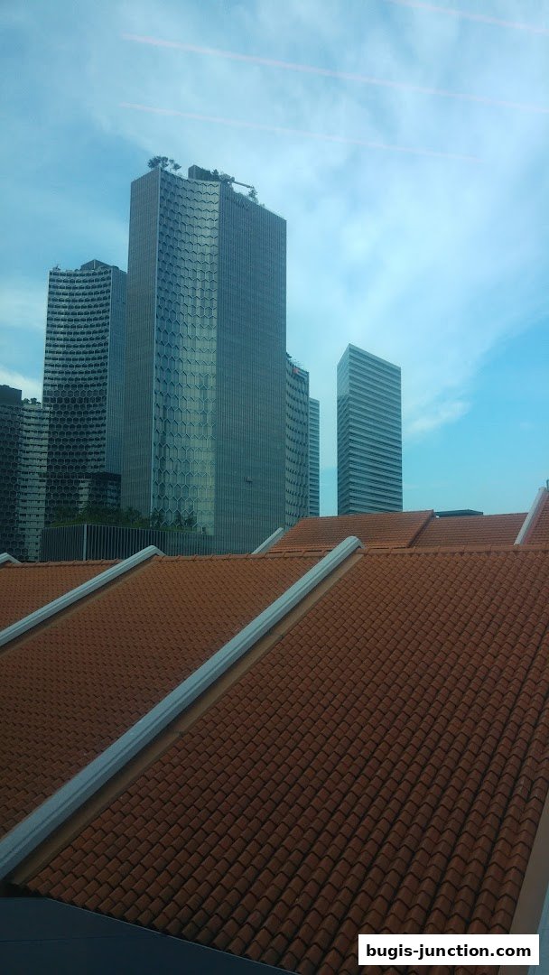 View of modern skyscrapers and tiled rooftops under a cloudy sky.