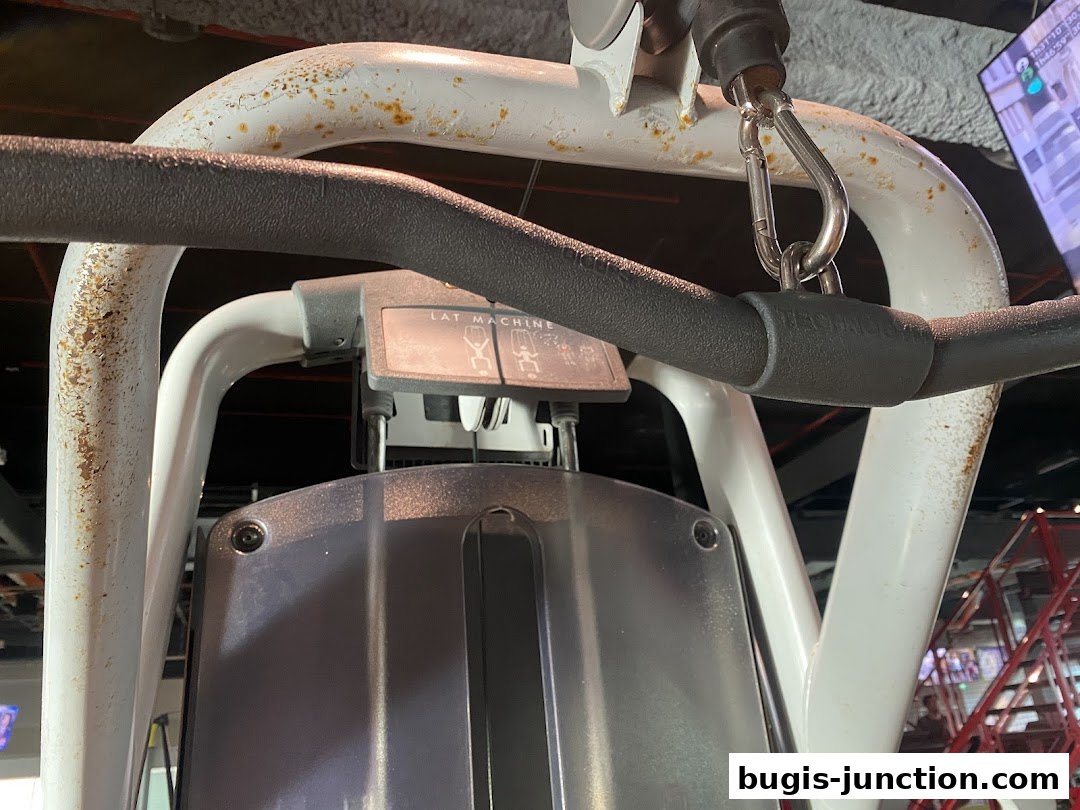 Close-up of a lat pulldown machine with a carabiner attached to the bar.