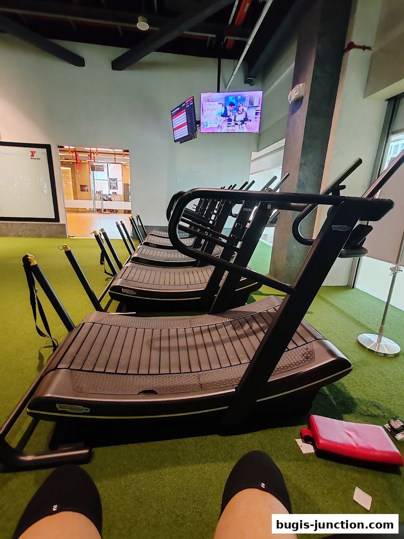Interior view of a gym with multiple treadmills and screens displaying fitness content.