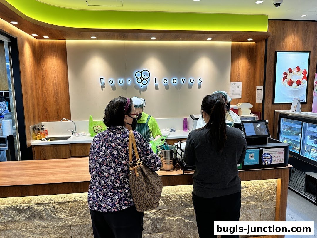 Customers ordering at the counter of a bakery with a cake display.