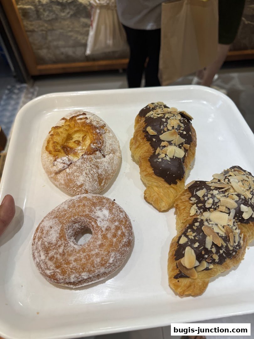 A white tray holds a variety of freshly baked pastries, including a dusted donut and chocolate-covered croissants.