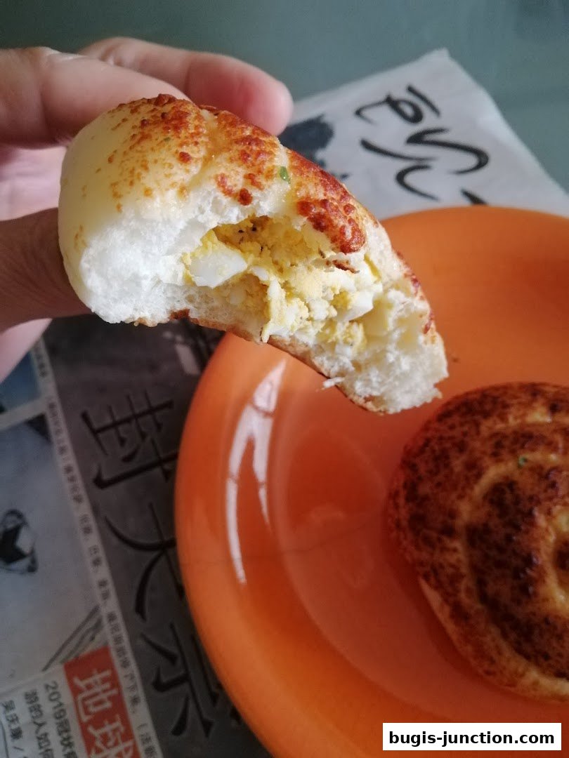 A hand holds a bite of a fluffy bread roll filled with scrambled eggs.