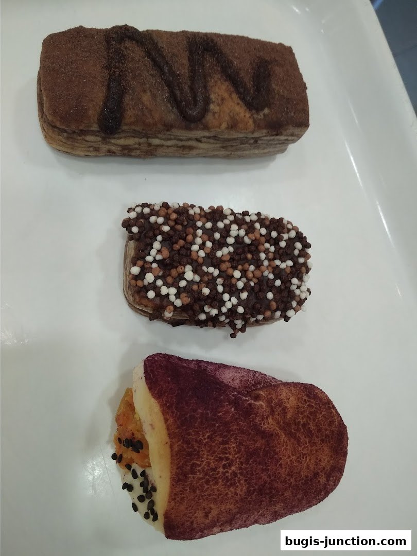 Three delicious pastries, one with chocolate drizzle, one with chocolate sprinkles, and one with purple topping.