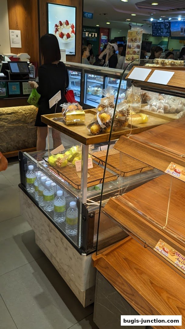 A bakery display case filled with pastries and bottled water, with customers in the background.