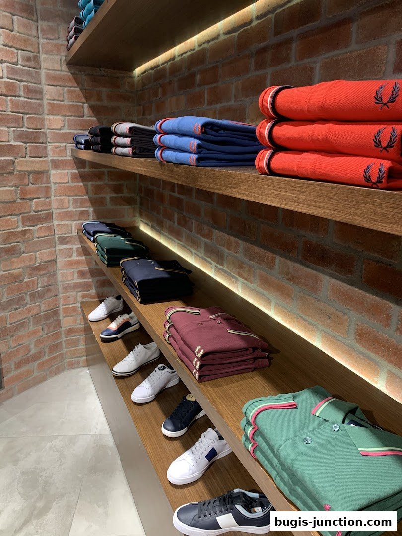 Neatly folded Fred Perry polo shirts and sneakers displayed on wooden shelves against a brick wall.