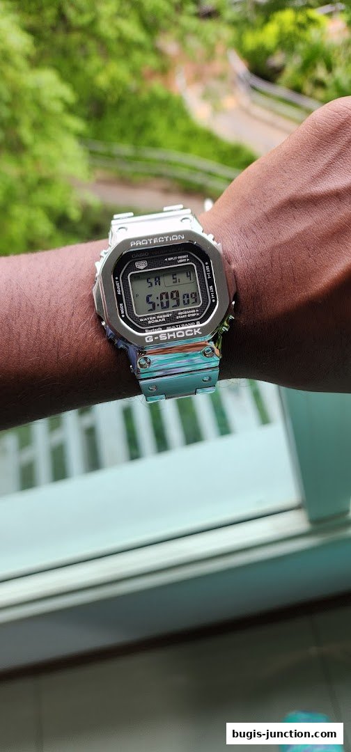 A person wears a silver G-SHOCK CASIO watch with a digital display.