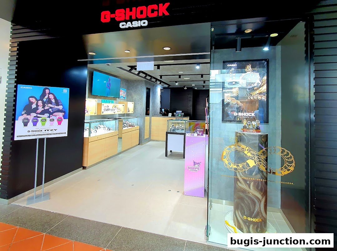 The entrance of a G-SHOCK CASIO watch store, showcasing display cases and promotional posters.