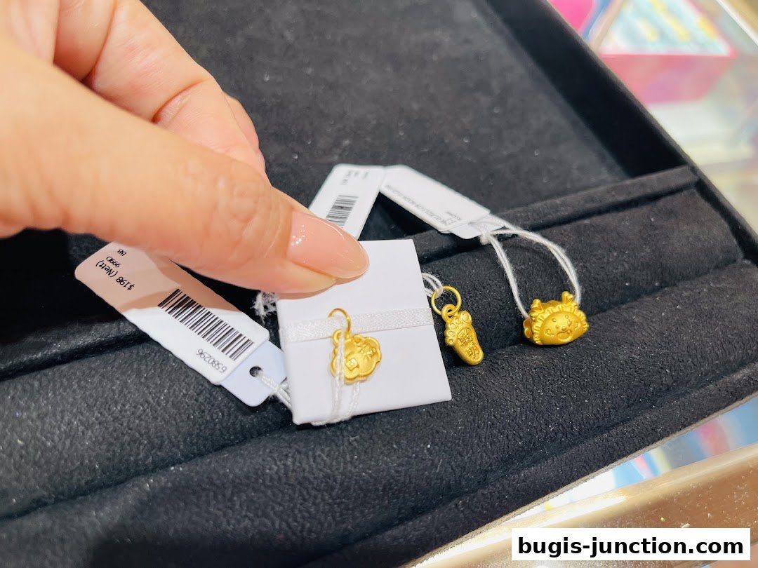 A hand holds a small gold charm with a price tag in a jewelry display.