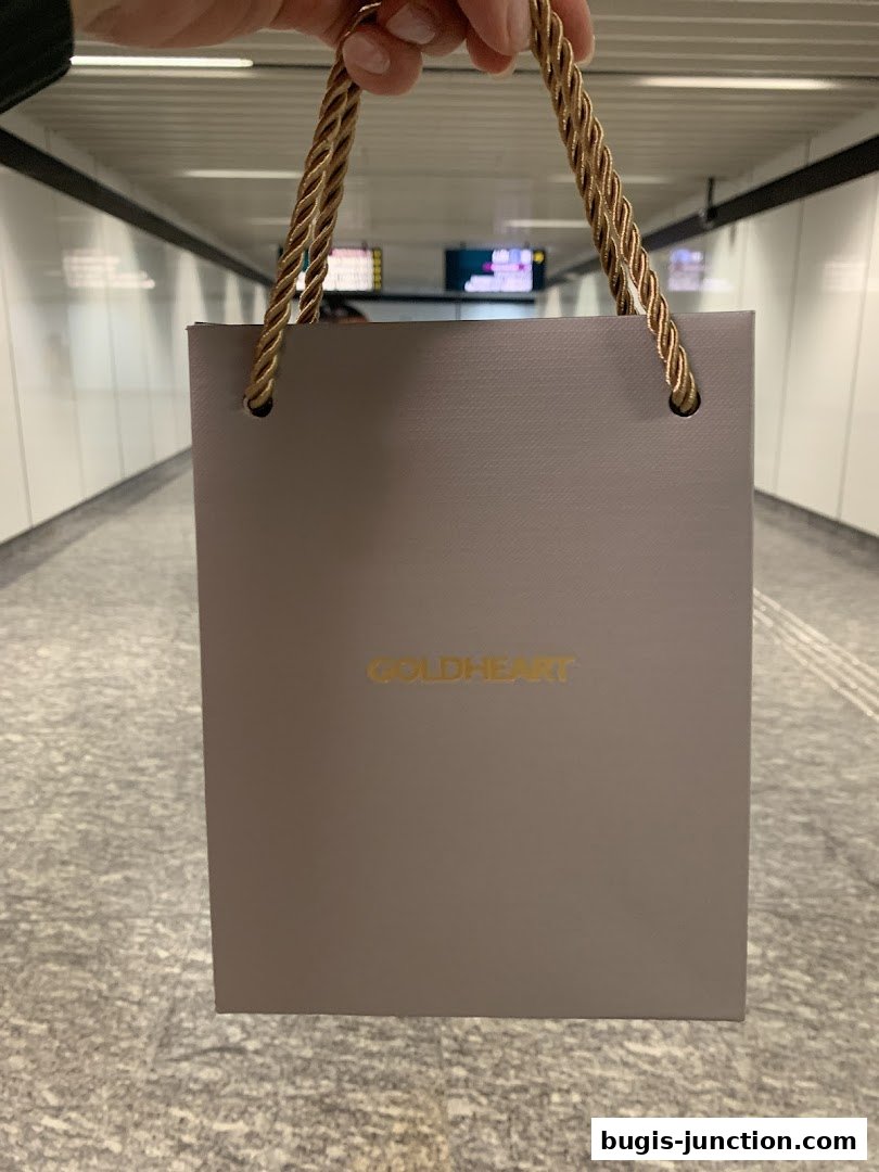 A person holds a Goldheart Jewelry shopping bag in a subway or tunnel.