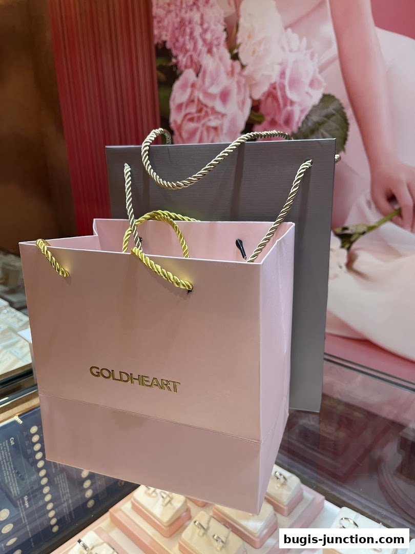 Goldheart Jewelry shopping bags displayed in front of a floral backdrop and display cases.