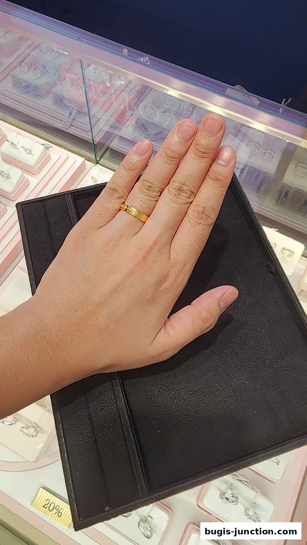 A hand wearing a gold ring is displayed in front of a jewelry display case.
