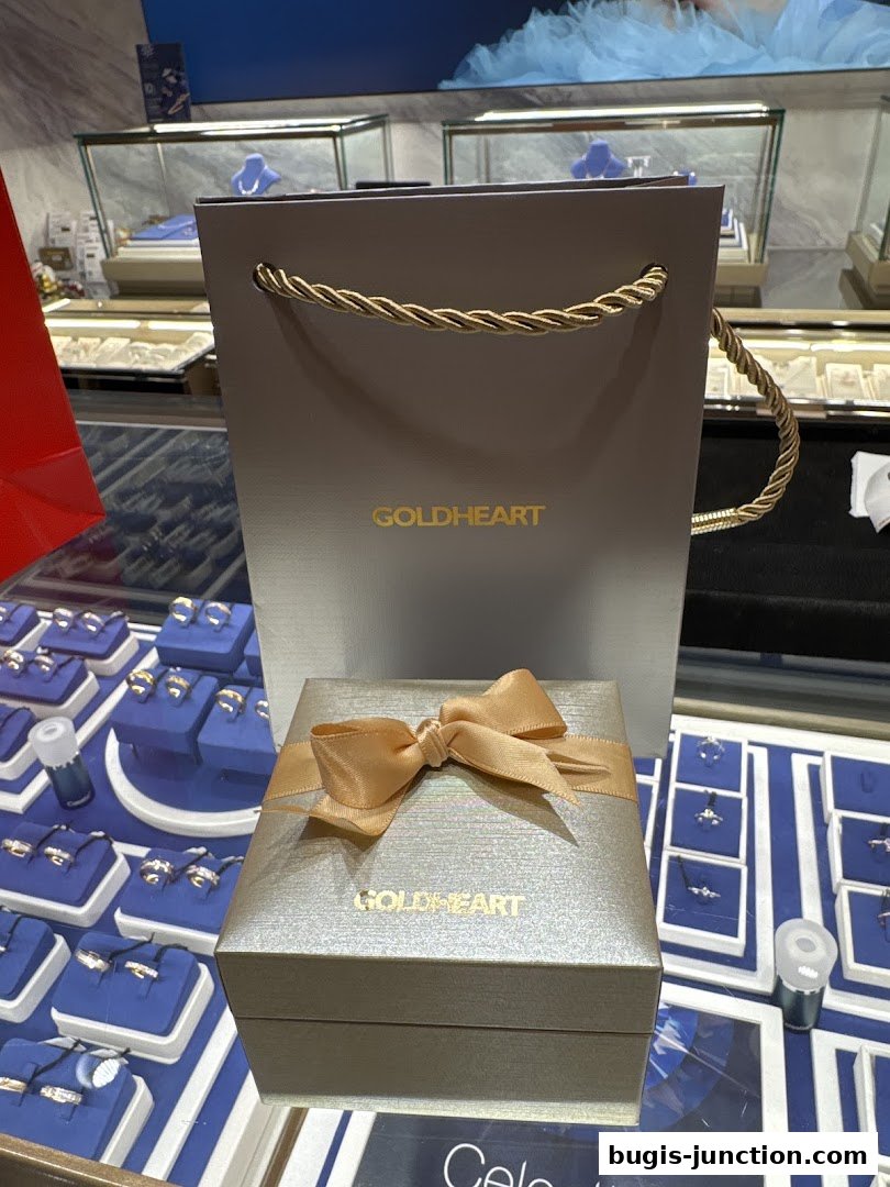 A Goldheart jewelry gift box and shopping bag displayed with rings in display cases.