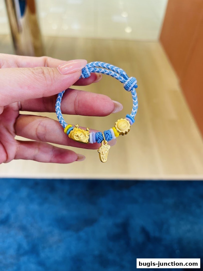 A hand holds a blue and white braided bracelet with gold charms.
