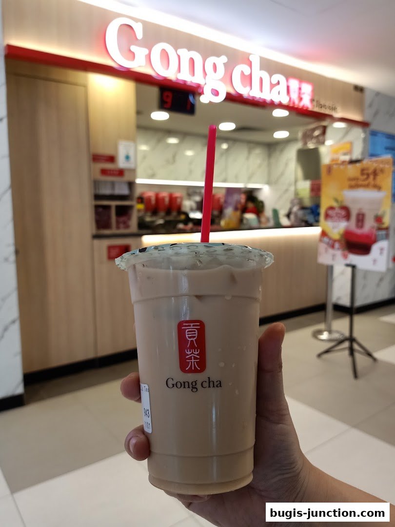 A hand holds a milk tea from Gong Cha with the shop's interior in the background.