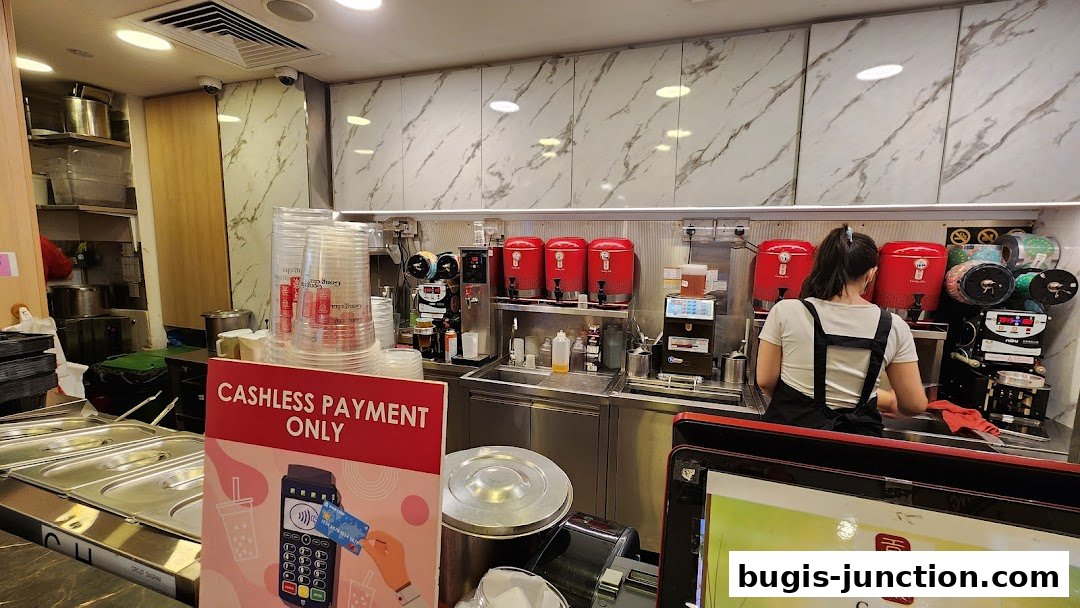 A worker prepares drinks behind a counter with beverage dispensers and cups at Gong Cha Classic.