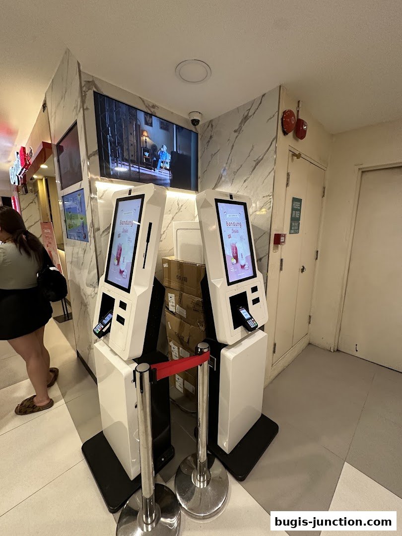 Two self-order kiosks are set up with a queue barrier in front of them.