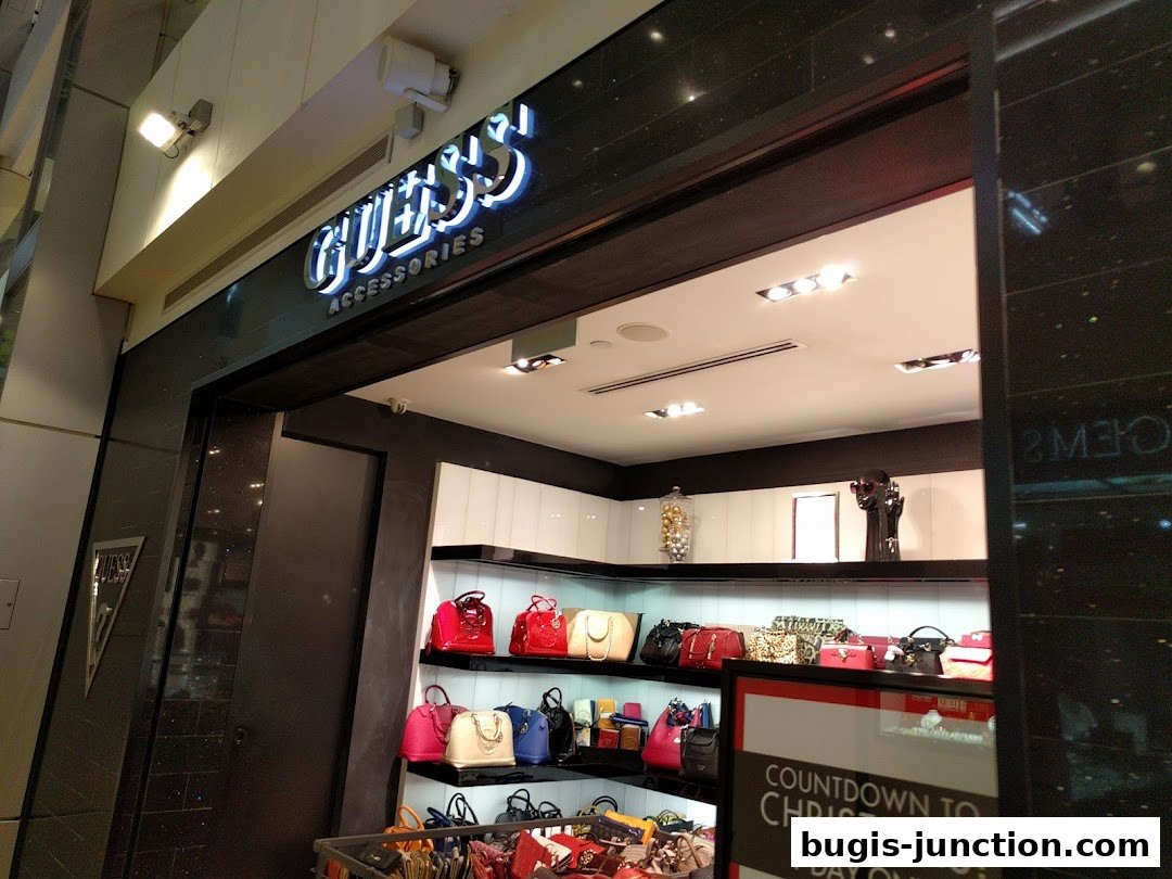 The entrance of a GUESS ACCESSORIES shop displaying various handbags on shelves.