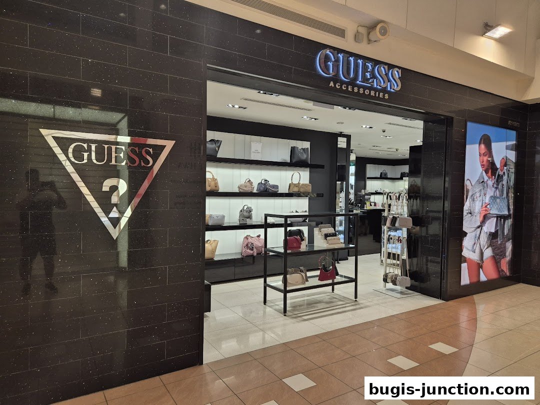 The entrance of a GUESS ACCESSORIES store, showcasing handbags and a fashion advertisement.