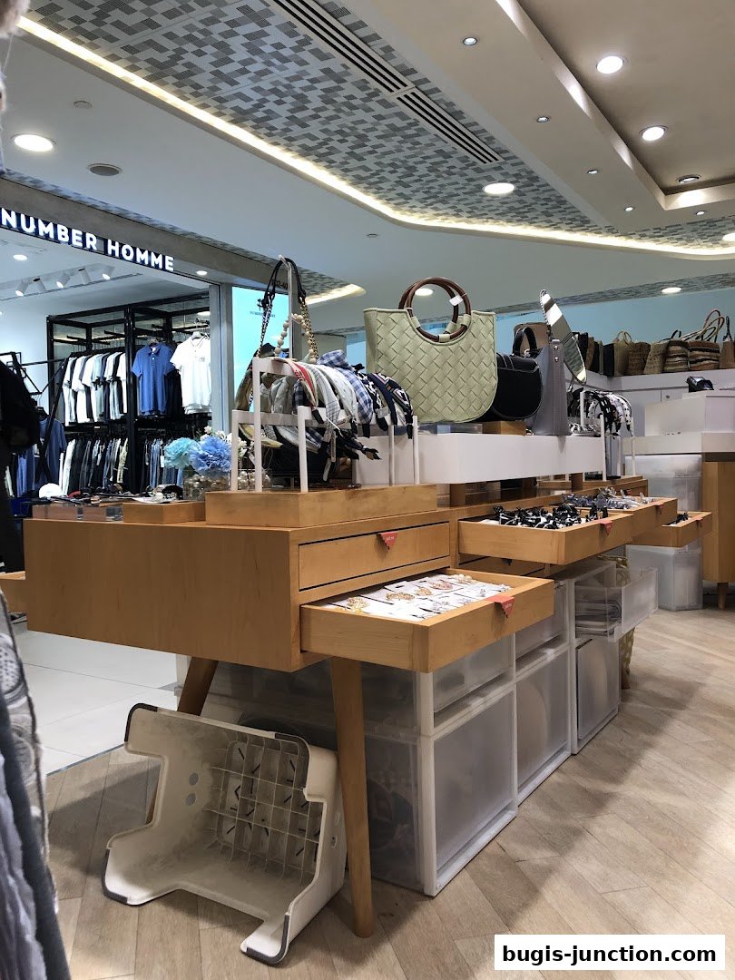A retail display featuring handbags, scarves, and jewelry, with clothing racks visible in the background.