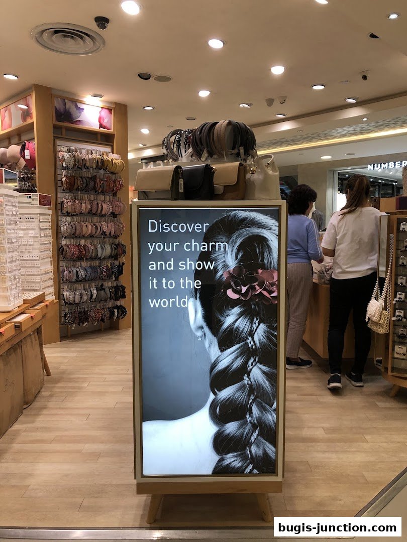 A shop interior displaying hair accessories and handbags, with a large illuminated advertisement.