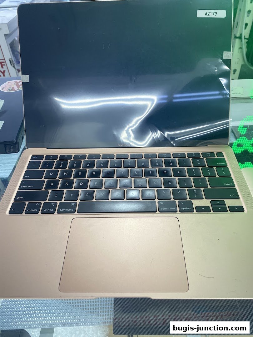 A close-up view of a gold MacBook laptop with a protective film on the screen.
