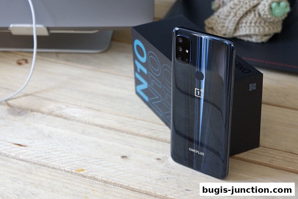 A black OnePlus N10 smartphone and its box are displayed on a wooden surface.