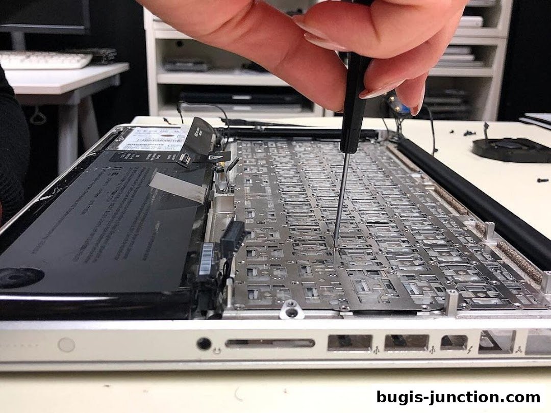 A close-up of a laptop being repaired, showing internal components and a hand with a screwdriver.