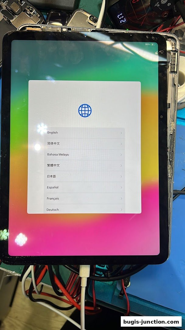 A tablet displaying a language selection screen, connected to charging cables.