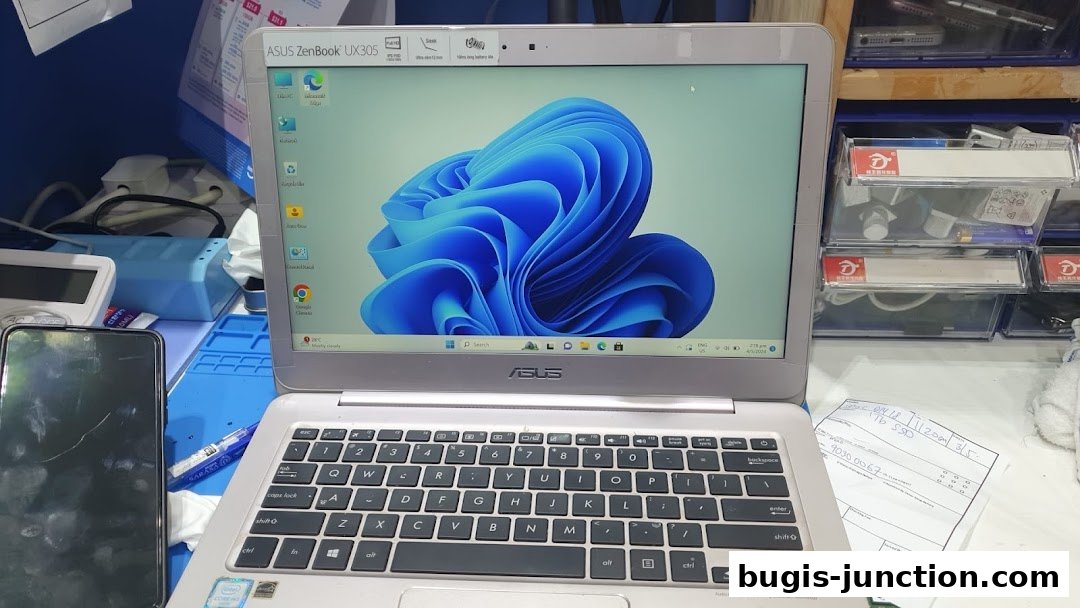 An ASUS ZenBook laptop is open, displaying Windows 11, next to a smartphone and repair parts.