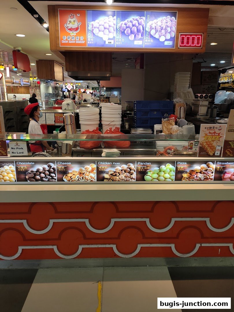 A food stall counter displaying various flavors of egg waffles with pictures and prices.