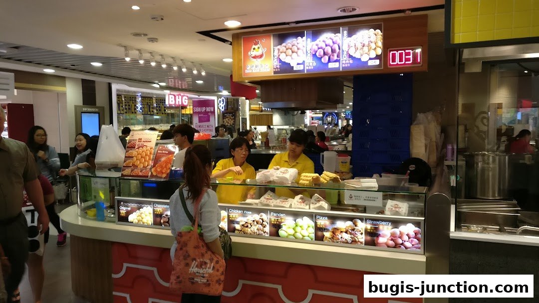 A food stall with staff serving customers, displaying various flavors of egg waffles.