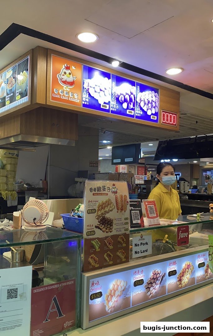 A food stall employee stands behind a counter displaying various flavors of Hong Kong egglets.