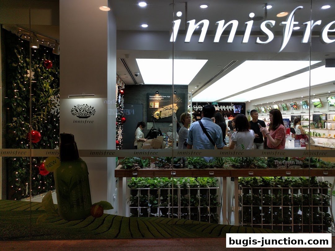 Innisfree Bugis Junction shop front with a display of plants and products, and customers inside.