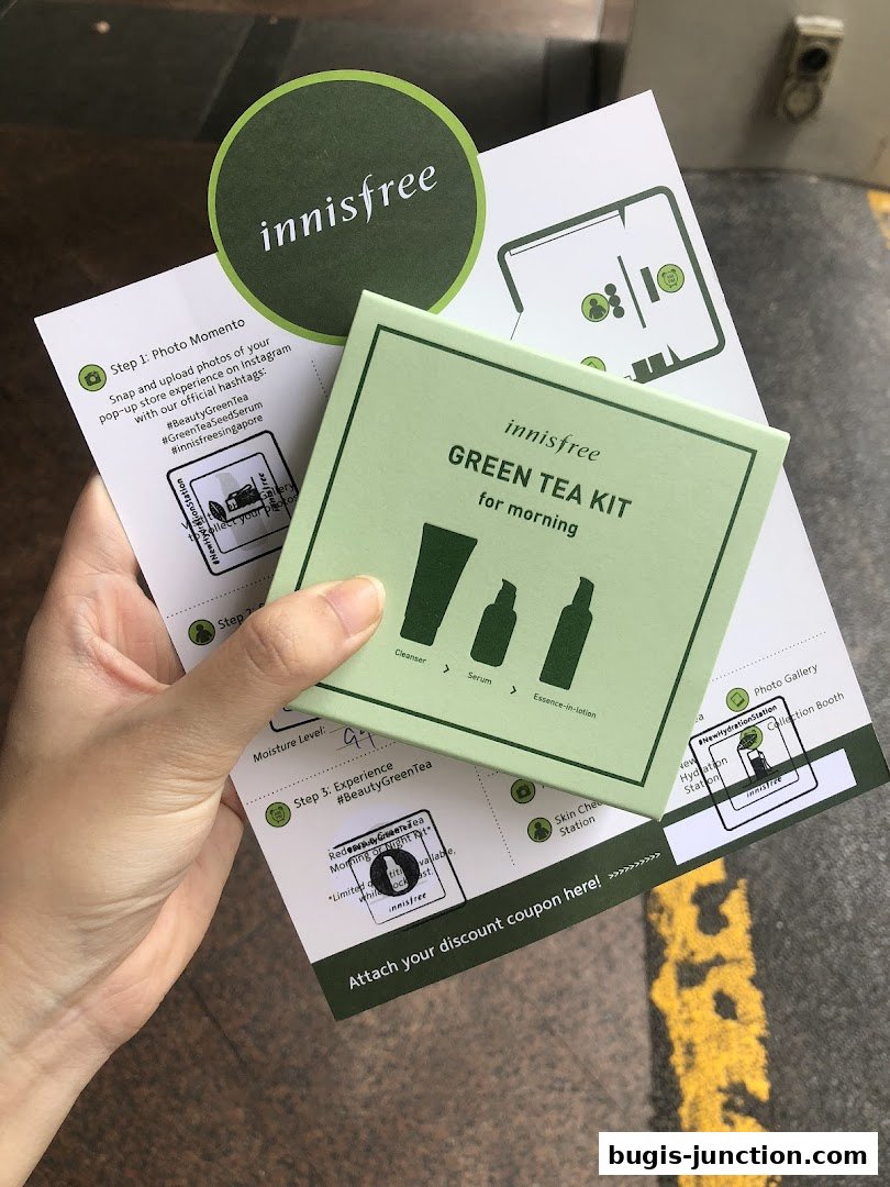 A hand holds an Innisfree Green Tea Kit and promotional materials.