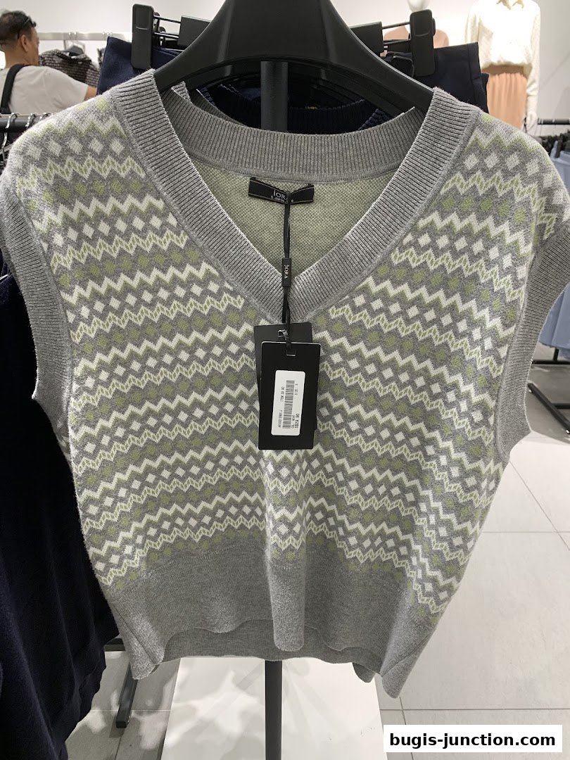 A grey sleeveless sweater with a green and white zigzag pattern, displayed on a hanger.