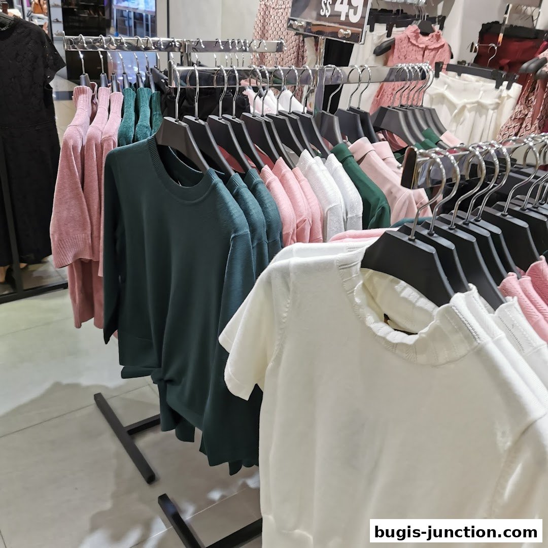 A rack of colorful women's tops and sweaters displayed in a retail store.