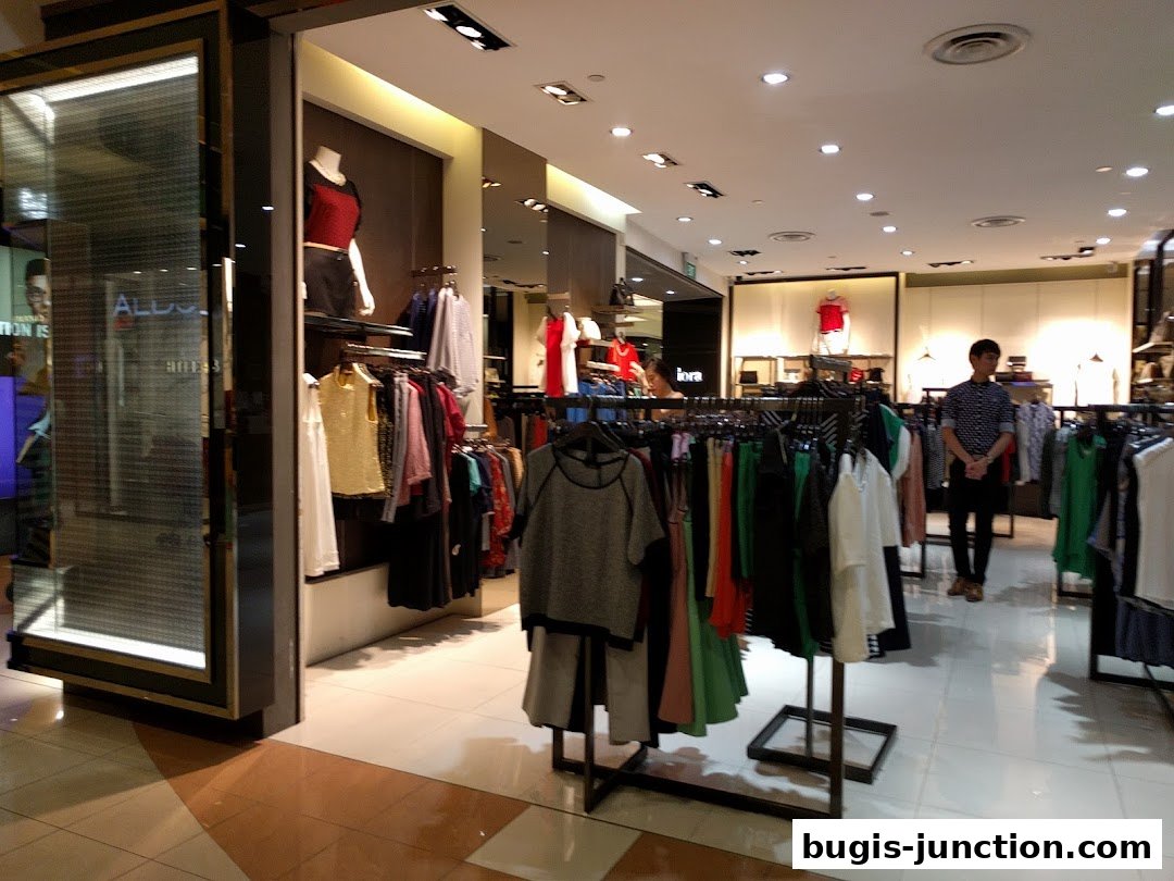 Interior view of a clothing store with racks of apparel and a male staff member.