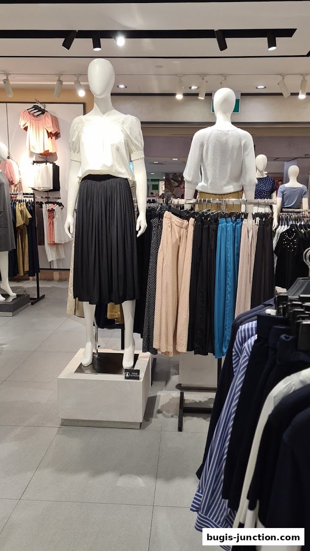Mannequins display stylish outfits with skirts and tops in a well-lit clothing store.