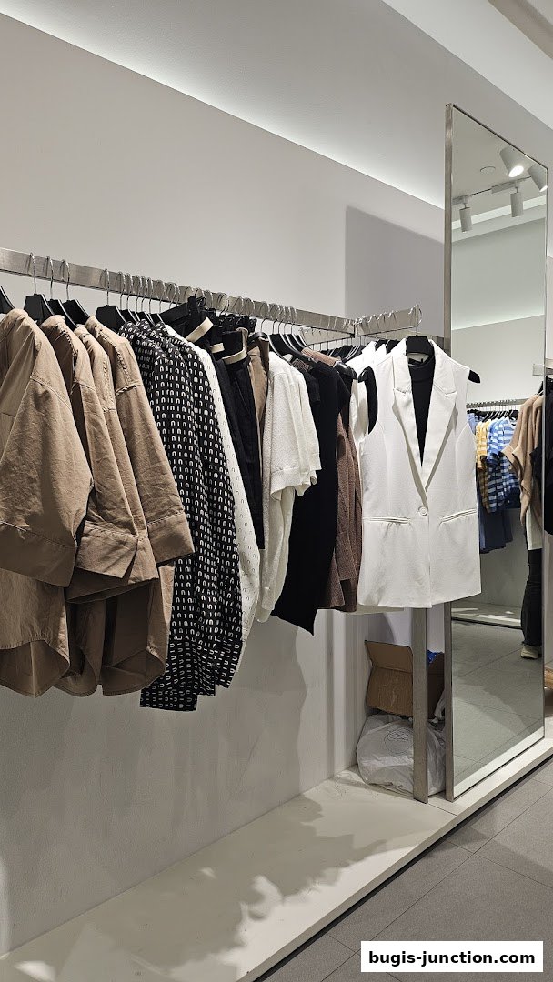 A rack of stylish women's clothing, including a white blazer, is displayed in a modern retail store.
