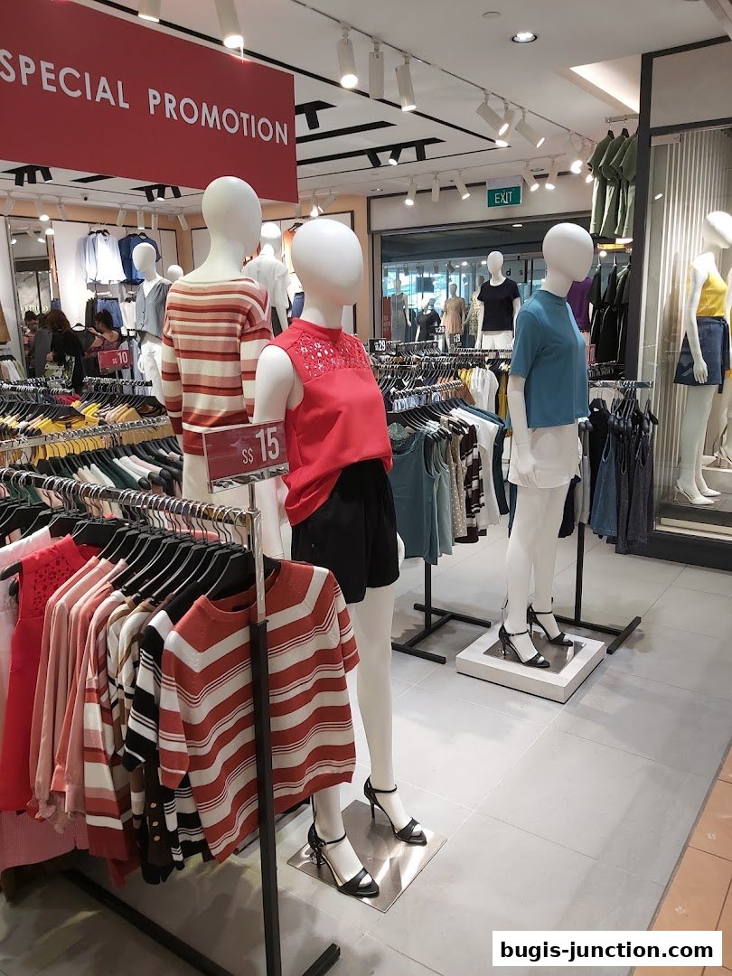 Mannequins display fashionable clothing in a brightly lit retail store with a special promotion banner.