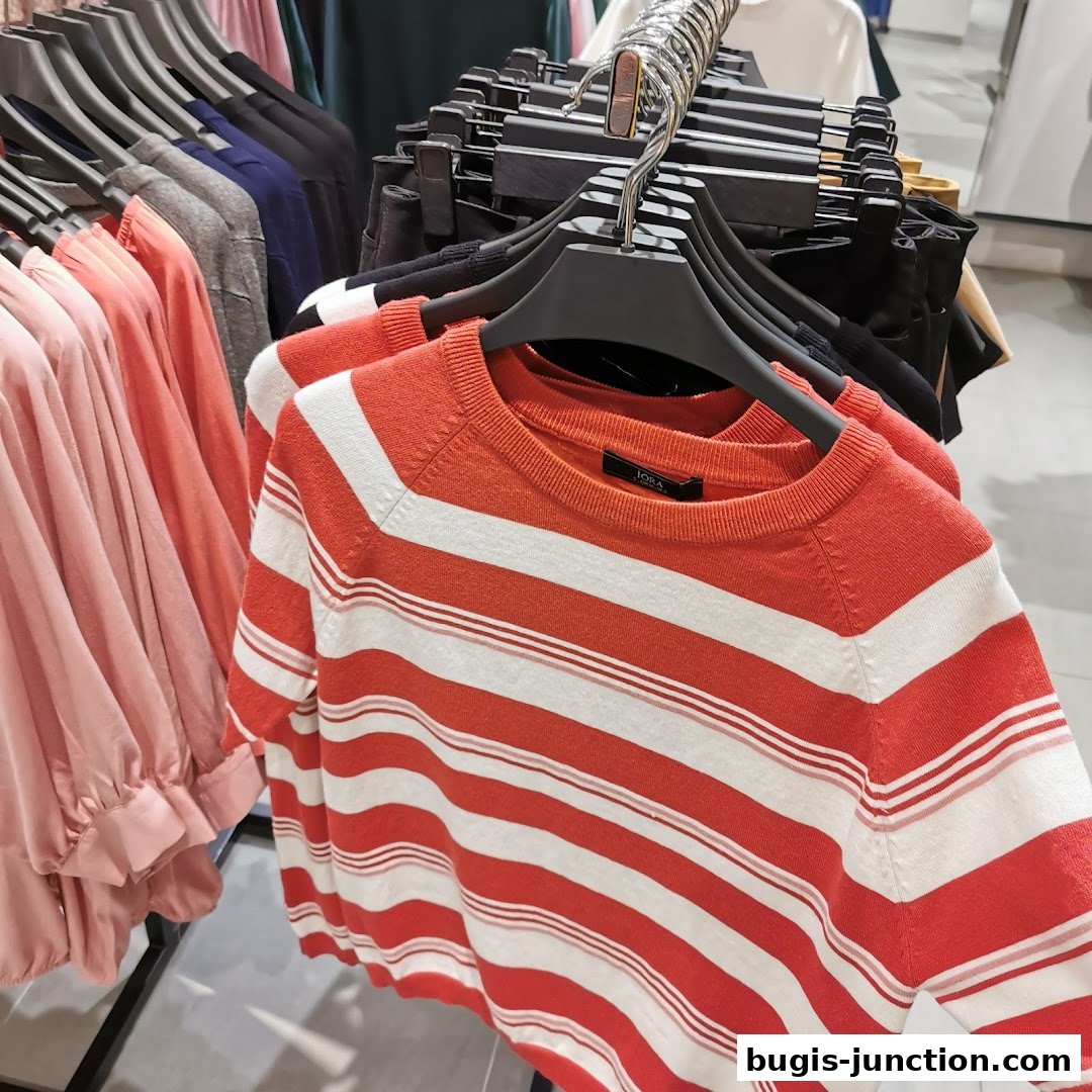 Close-up of striped sweaters and pink blouses on hangers in a retail store.