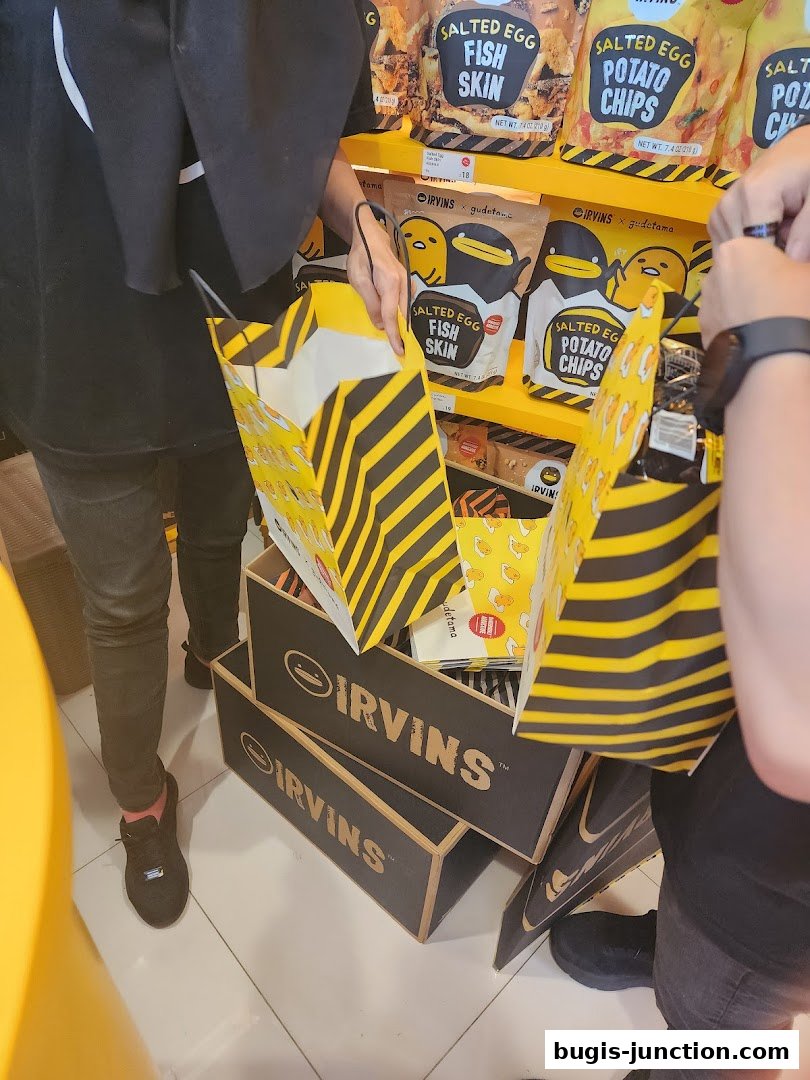People holding shopping bags at IRVINS, with shelves of salted egg snacks in the background.