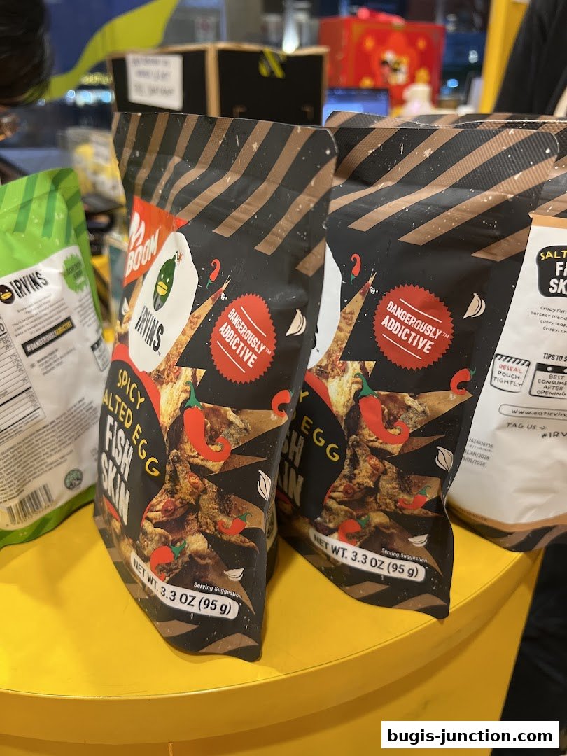 Bags of IRVINS Spicy Salted Egg Fish Skin snacks displayed on a yellow surface.