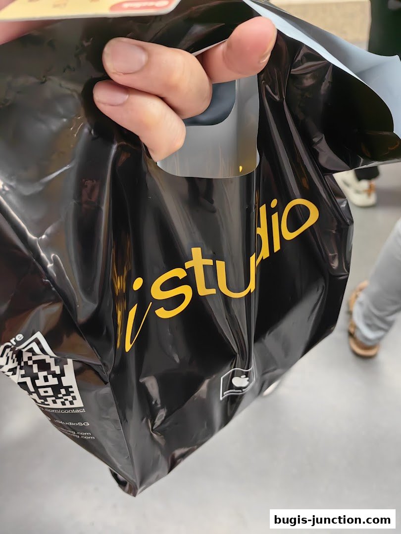 A hand holds a black shopping bag with the yellow 'iStudio' logo and an Apple logo.